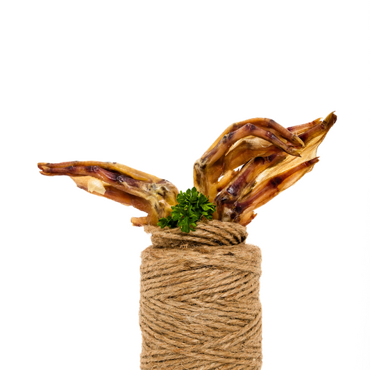 Three dehydrated duck feet from Wild Nosh Pets, rich in glucosamine and chondroitin, with a sprig of parsley, are arranged on a roll of twine against a white background.