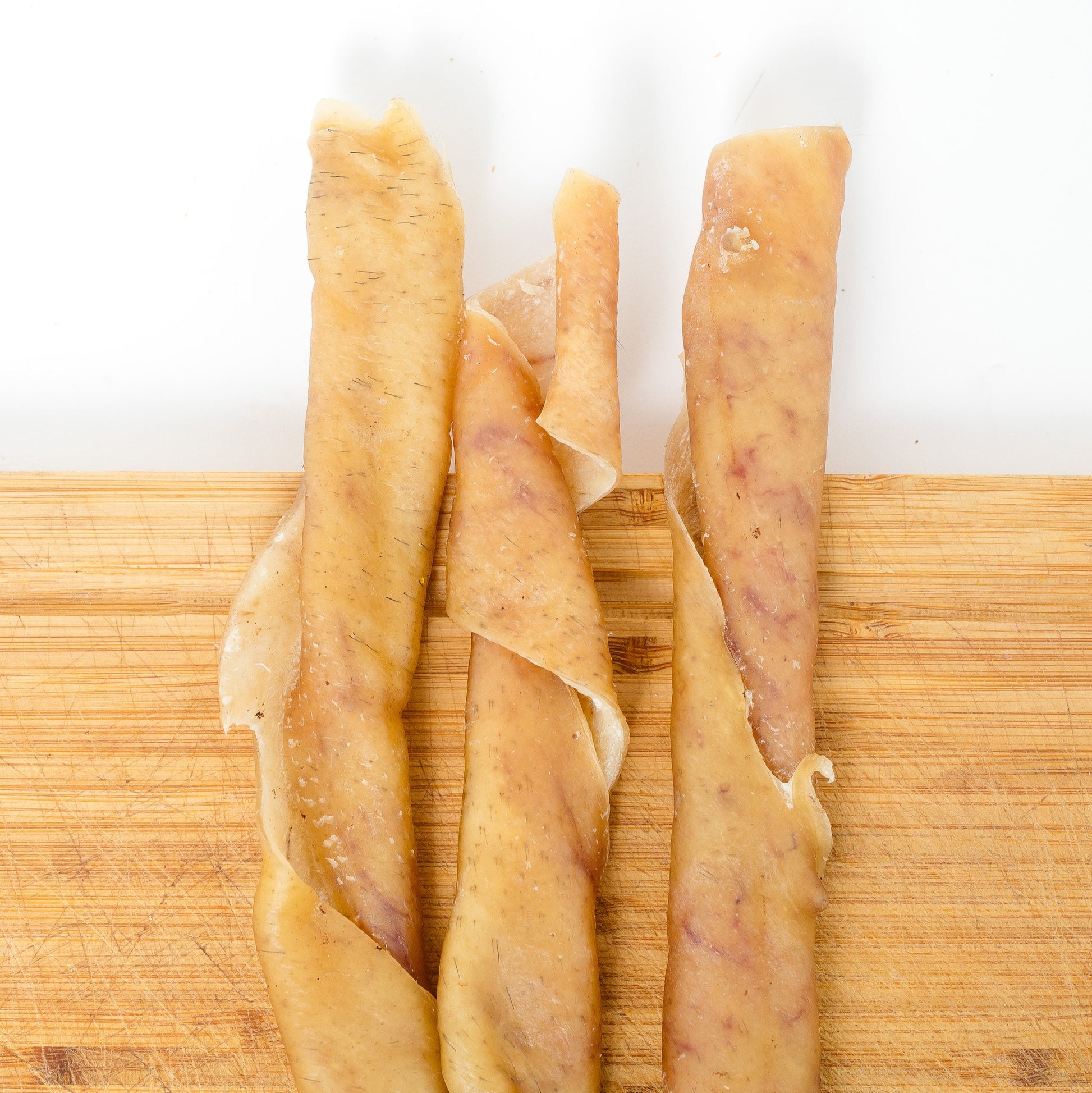 Three Heritage Breed Dehydrated Pork Rolls by Wild Nosh Pets are arranged on a wooden cutting board against a white background.