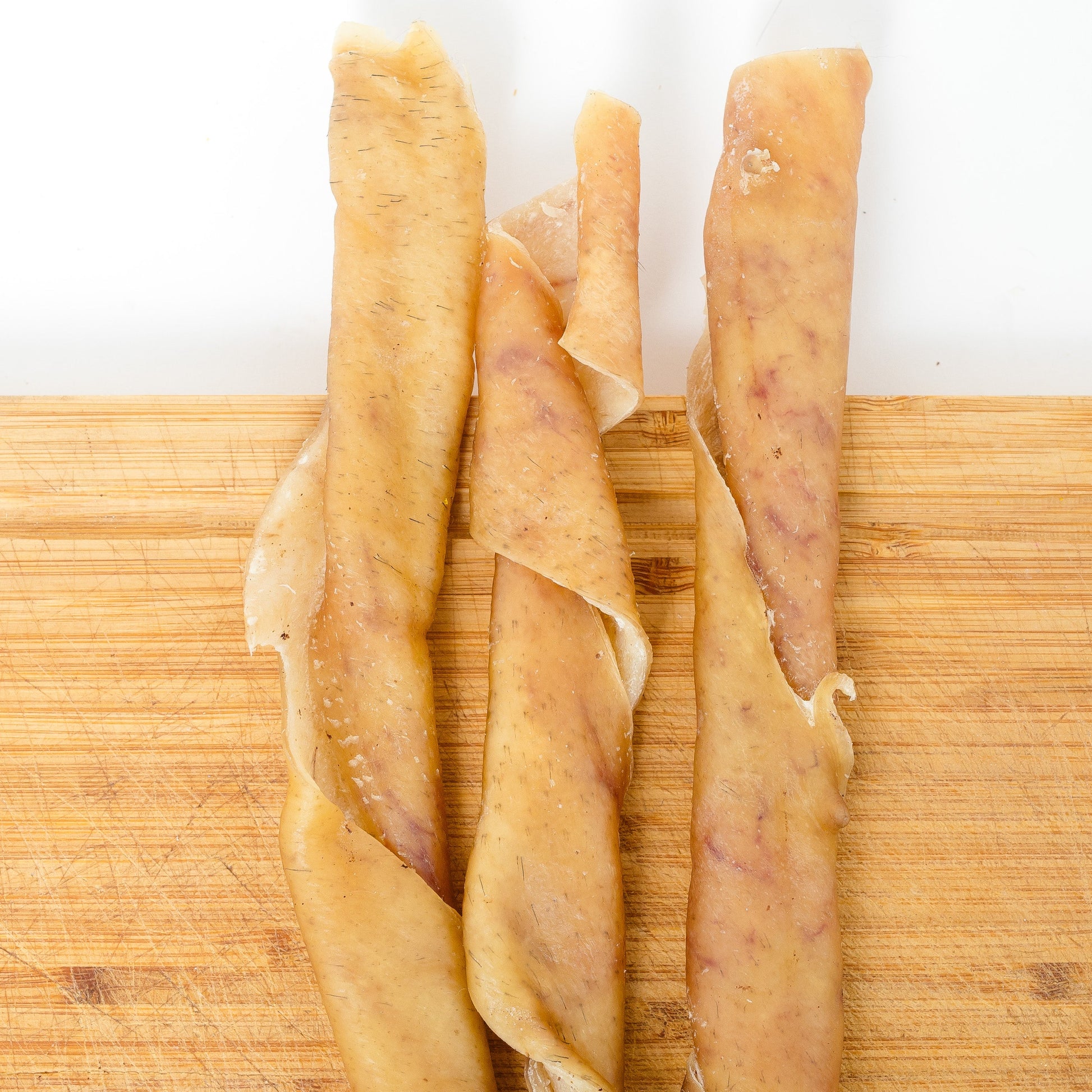 Three Heritage Breed Dehydrated Pork Rolls from Wild Nosh Pets are arranged side by side on a wooden surface.