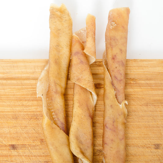 Three Heritage Breed Dehydrated Pork Rolls from Wild Nosh Pets are arranged side by side on a wooden surface.