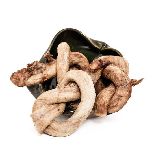 A ceramic bowl tipped over, spilling several large Wild Nosh Pets Freeze-Dried Bison Bully Pretzels onto a white background.