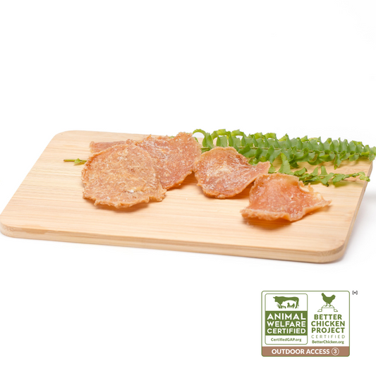 A cutting board with pieces of Wild Nosh Pets Chicken Crispers 1 oz and a garnish. Label shows Animal Welfare Certified and Better Chicken Commitment certifications, highlighting the use of heritage breed chickens with outdoor access.