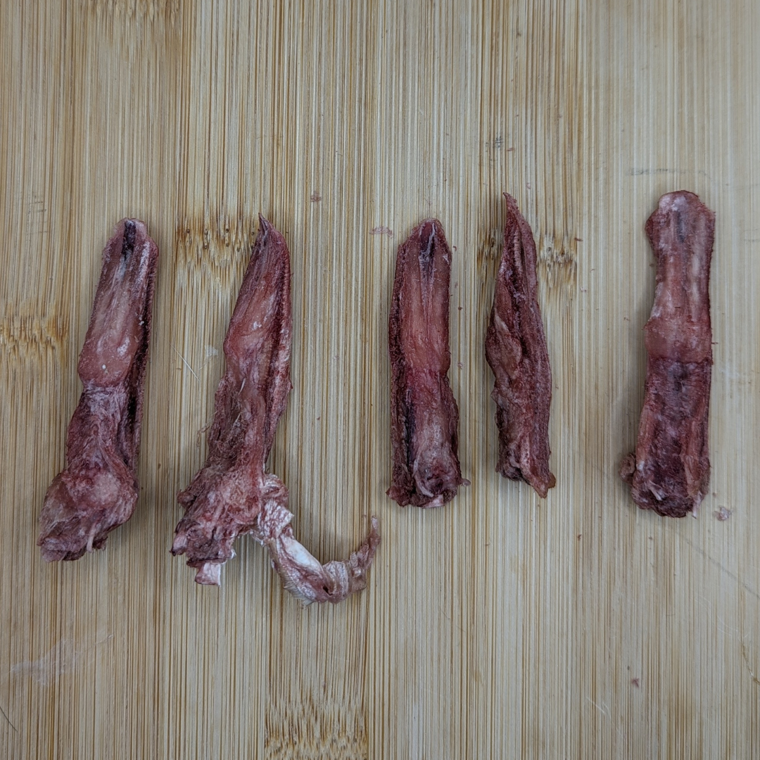 Five pieces of protein-packed dried meat are arranged on a wooden surface, making this an ideal dog chew. Wild Nosh Pets Freeze-dried Duck Tongues 1oz will surely delight your furry friend!