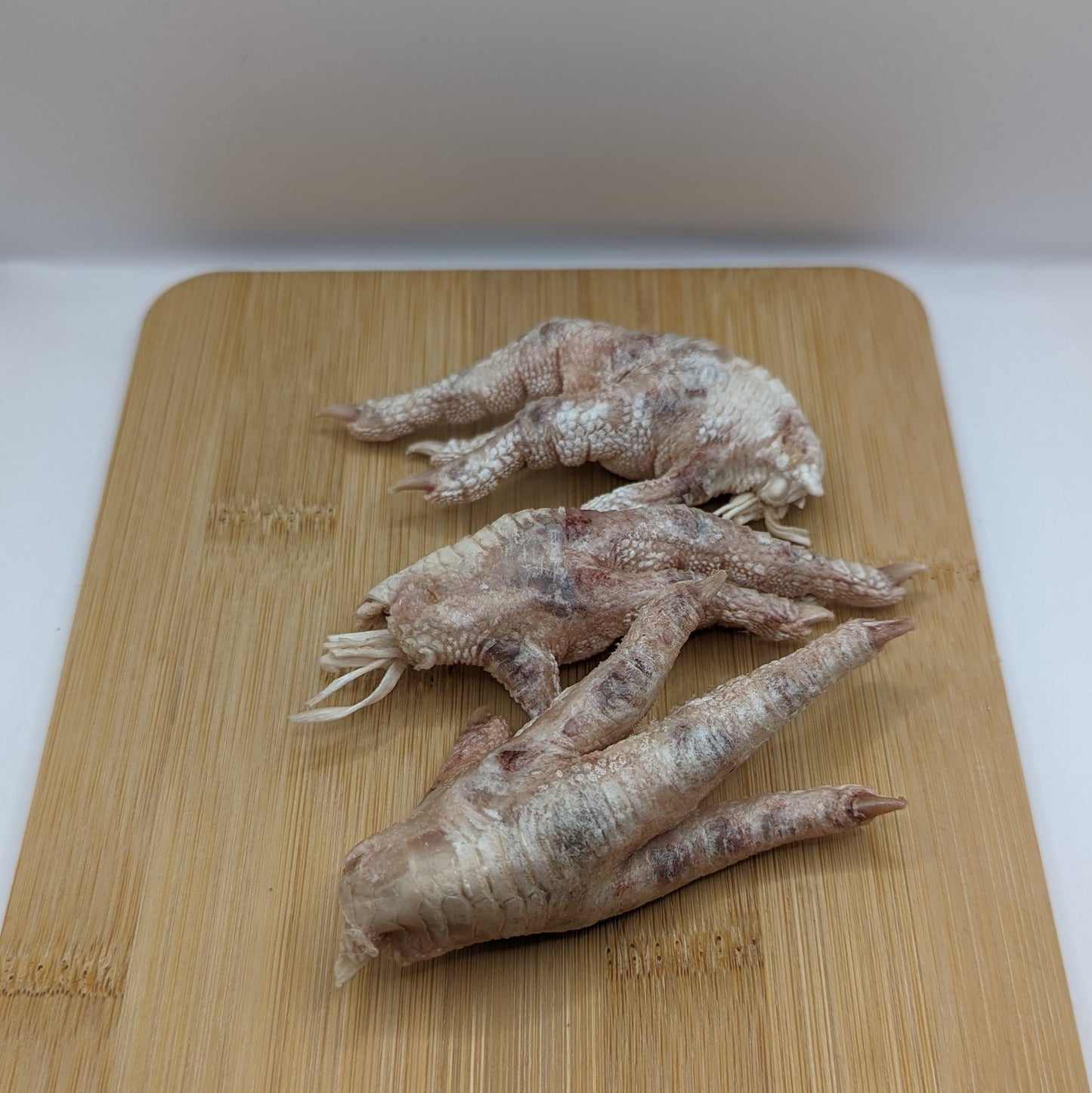 Three Wild Nosh Pets Freeze-Dried Chicken Feet rest on a wooden cutting board.