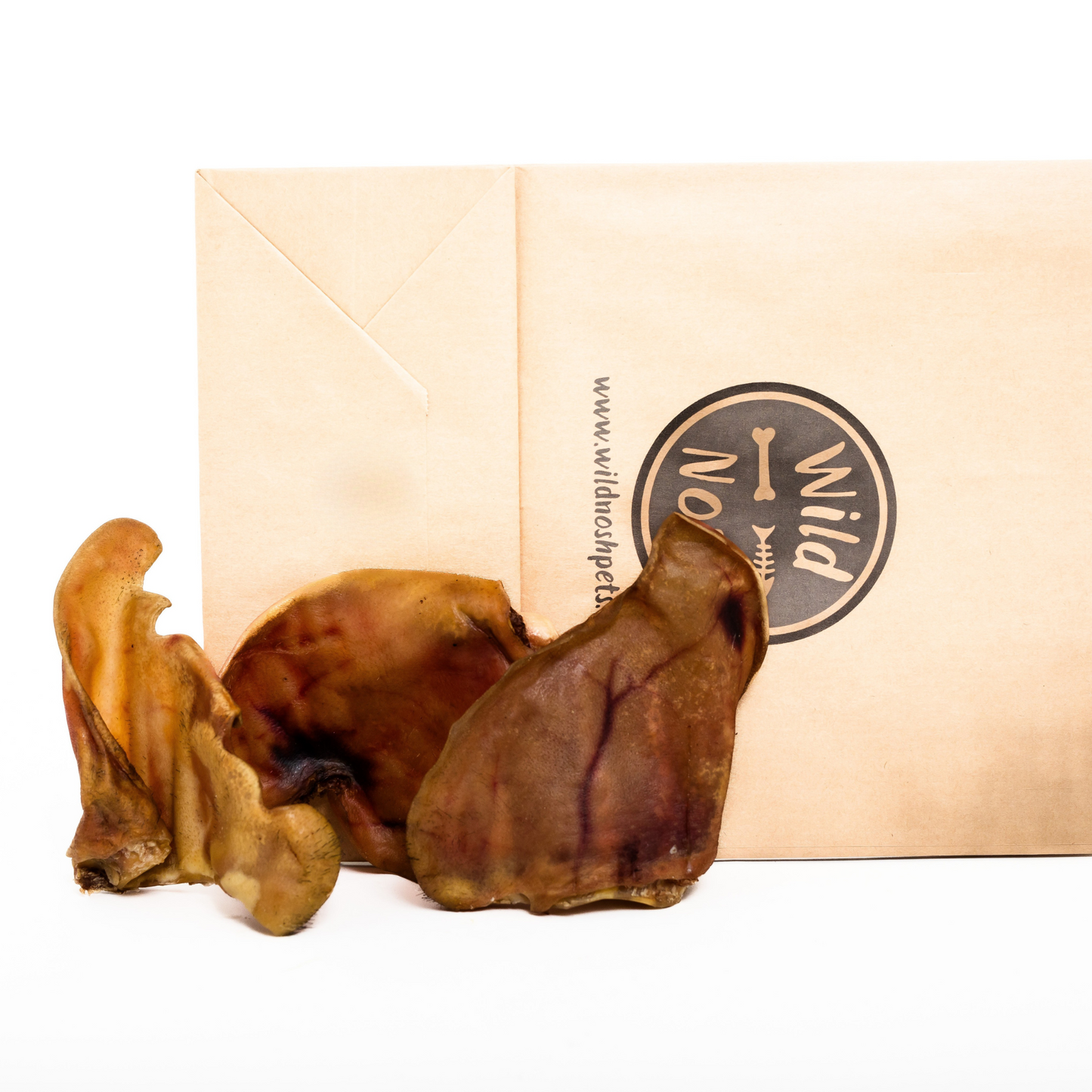 Two Heritage Breed Dehydrated Pig Ears from Wild Nosh Pets are shown in front of a beige envelope featuring the "Wild" logo and website, making a perfect natural dog chew.