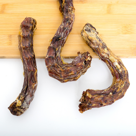 Wild Nosh Pets Dehydrated Duck Neck—three dried duck necks on a white surface with a wooden cutting board in the background—offer natural protein to support your pet’s joint health.
