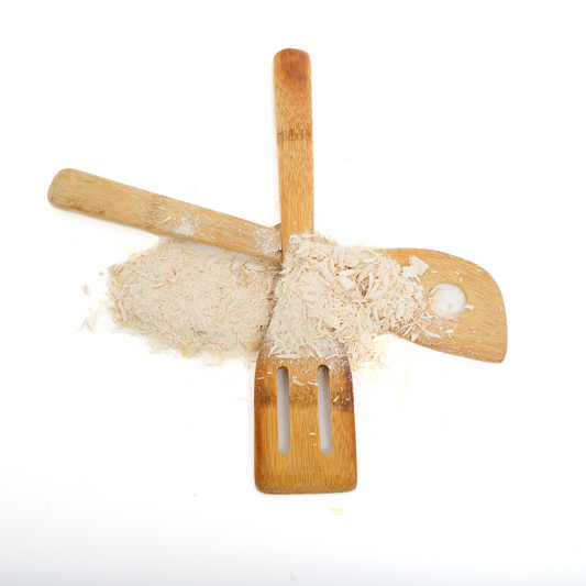 Two wooden kitchen utensils arranged in an X shape with a pile of Wild Nosh Pets Freeze-Dried Chicken Pawmesan Topper (1oz) scattered on top, perfect for picky eaters, against a white background.