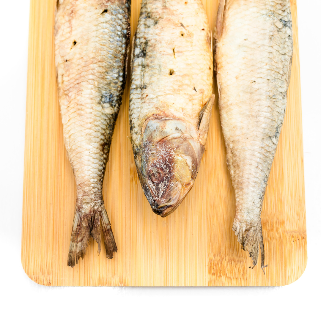 Three whole Wild Nosh Pets Freeze-Dried Sardine cat treats are arranged side by side on a wooden cutting board with a white background.