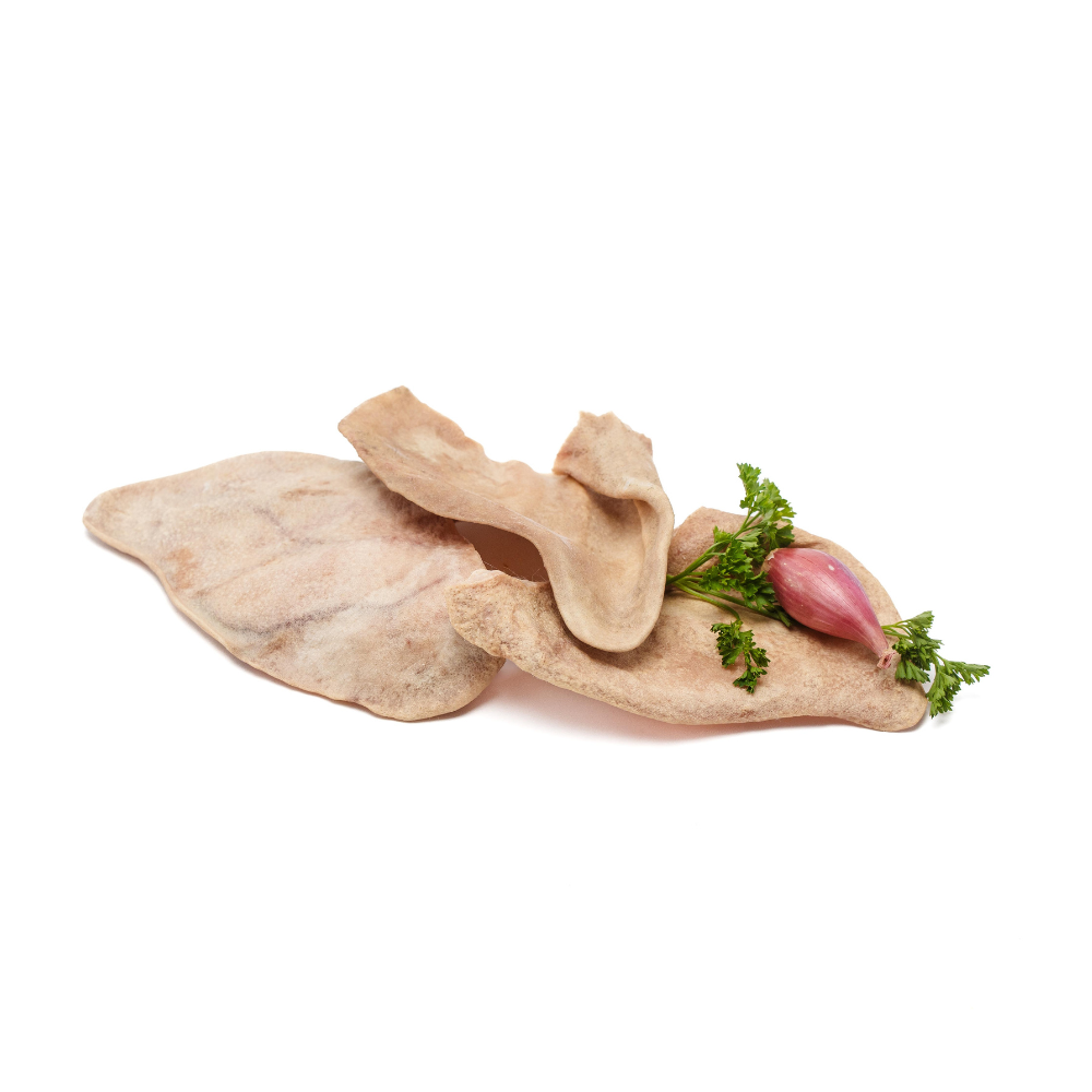 Two Heritage Breed Freeze-Dried Pig Ears from Wild Nosh Pets with a sprig of parsley and a small red bulb, possibly garlic, placed on top, offering glucosamine and chondroitin benefits.