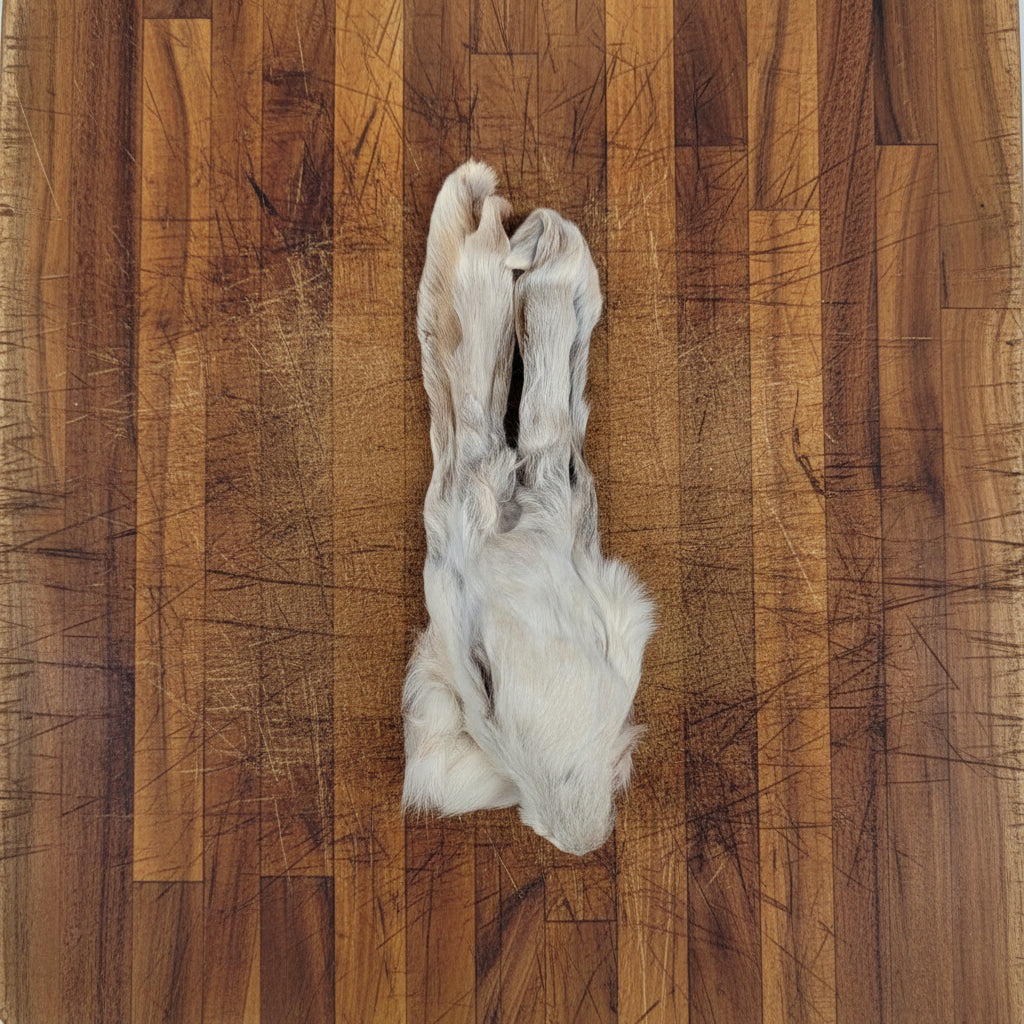 A dehydrated rabbit head with fur by Wild Nosh Pets sits on a wooden cutting board—an unusual long-lasting chew or treat for cats.