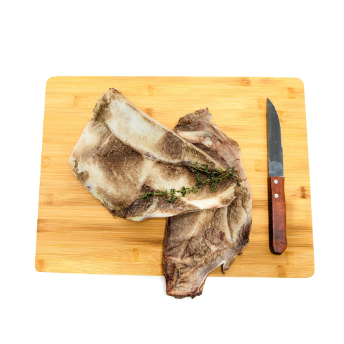 Two pieces of Freeze-Dried Bison Scapula by Wild Nosh Pets garnished with fresh thyme on a wooden cutting board, accompanied by a knife with a wooden handle, perfect for those teething puppies looking for a savory chew.