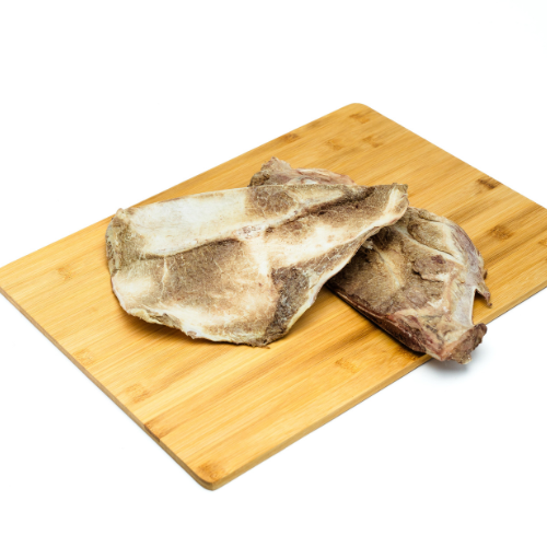 Two pieces of Wild Nosh Pets Freeze-Dried Bison Scapula placed on a wooden cutting board against a white background, perfect for teething puppies or senior dogs in need of a nutritious snack.