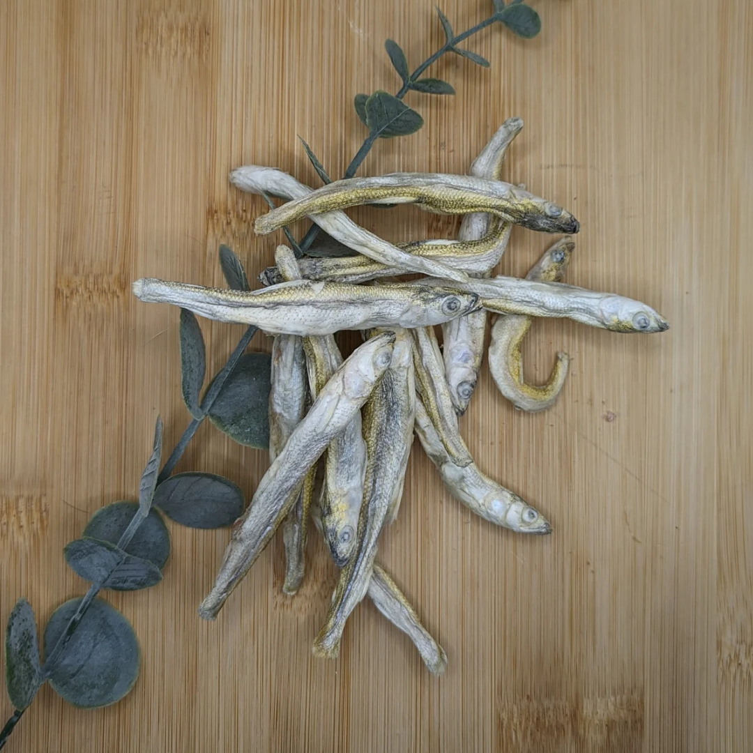 Several Wild Nosh Pets Freeze-dried Smelt 1oz laid out on a wooden surface, accompanied by green leaves, highlighting the benefits of Omega-3 fatty acids.