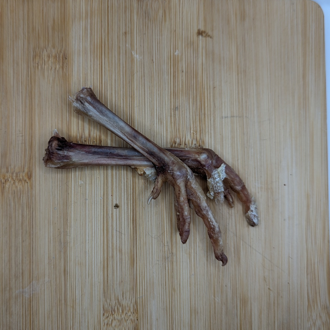 Two Freeze-Dried Pheasant Feet from Wild Nosh Pets, rich in glucosamine and chondroitin, are placed on a wooden cutting board.