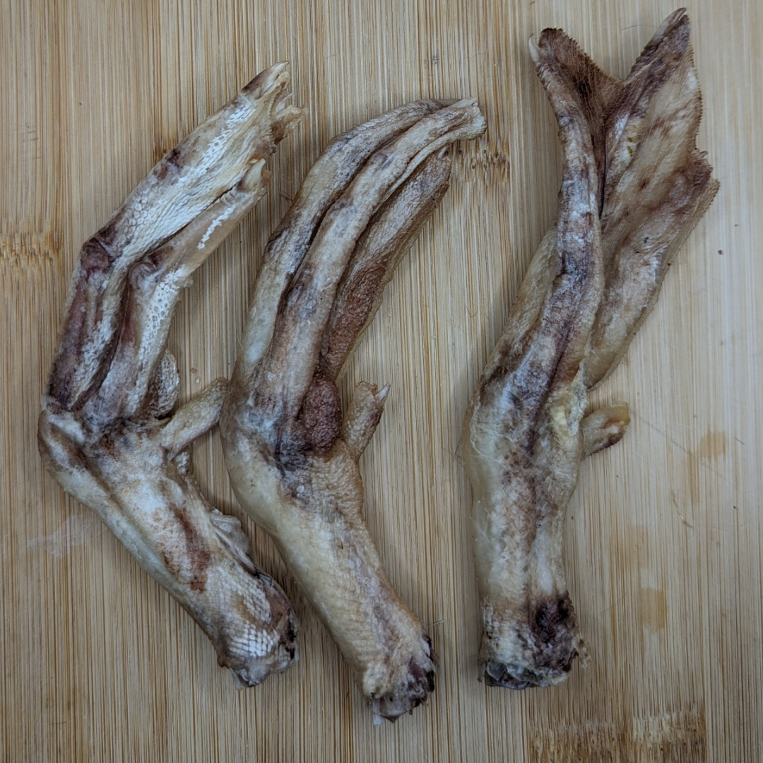 Three dried, brown Freeze-Dried Duck Feet from Wild Nosh Pets arranged on a light wooden surface, perfect for providing senior dogs with a natural treat that may help alleviate arthritis.