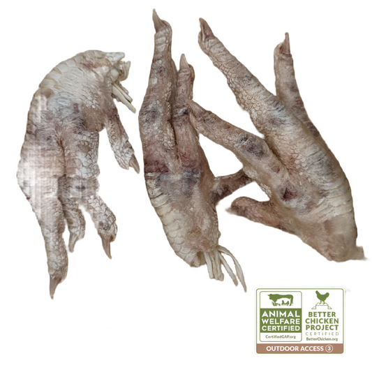 Three raw Wild Nosh Pets Freeze-Dried Chicken Feet on a wooden surface, accompanied by certification labels: Animal Welfare Certified and Better Chicken Commitment.