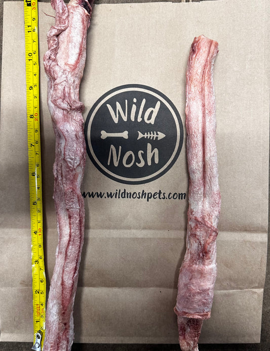 A pair of protein-rich chews of varying lengths are placed on a Wild Nosh Pets paper bag, with a measuring tape next to them. These 10-12" Freeze Dried Bison Bully Sticks come from North American grasslands, guaranteeing both quality and taste for your pet.