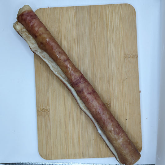 A long sausage-like food item, made from heritage breed pigs, is placed on a rectangular wooden cutting board. This product is known as Heritage Breed Dehydrated Pork Rolls by Wild Nosh Pets.