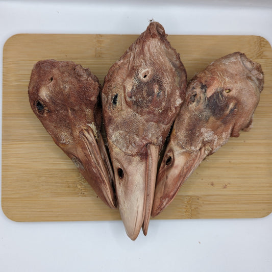 Three Wild Nosh Pets Freeze-Dried Duck Heads arranged on a wooden cutting board, offering a nutritious treat and crunchy snack for dogs.