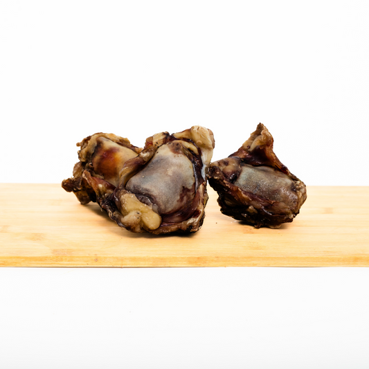 Two Smoked Bison Knee Cap bones from Wild Nosh Pets are displayed on a wooden cutting board against a plain white background.