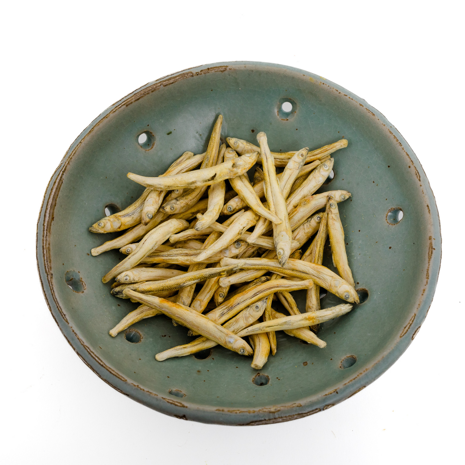 A green ceramic bowl filled with Wild Nosh Pets Freeze-Dried Smelt 1 oz., viewed from above on a white background—a tasty, natural treat and excellent source of Omega-3 fatty acids for your pet.