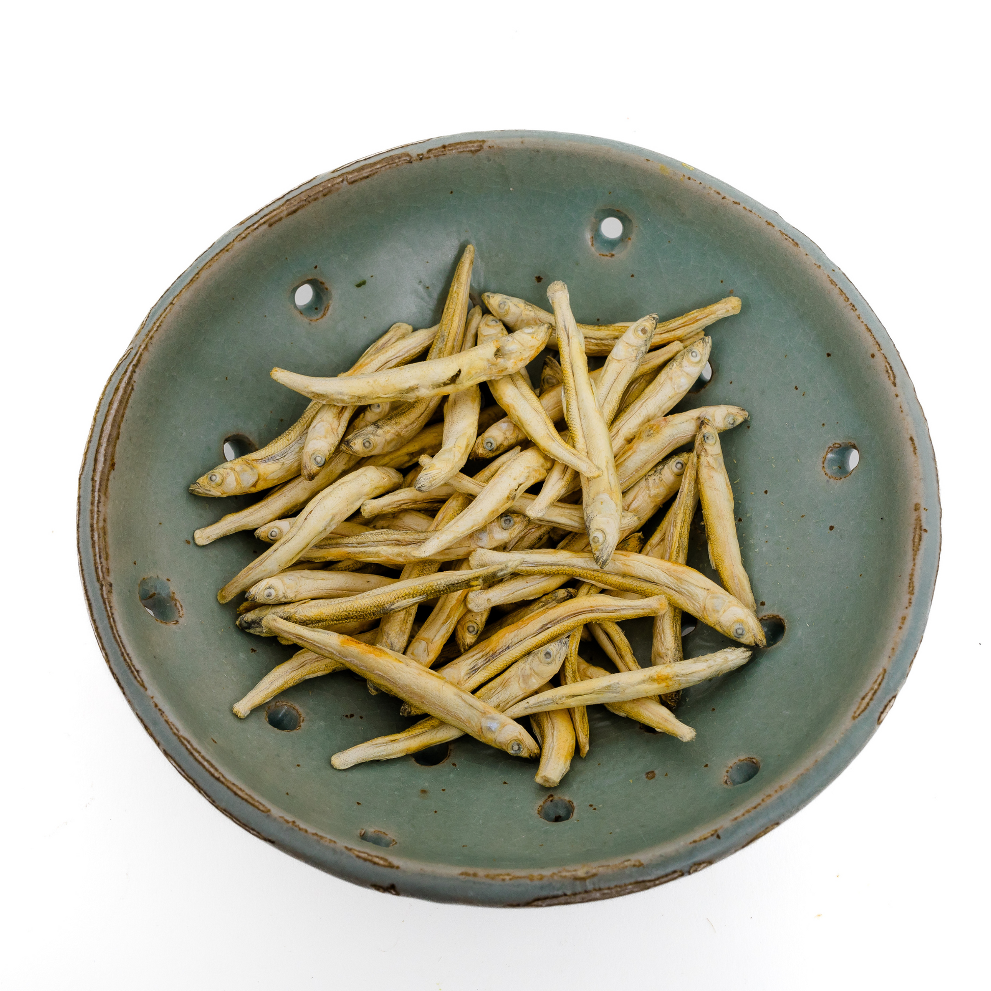 A green ceramic bowl filled with Wild Nosh Pets Freeze-Dried Smelt 1 oz., viewed from above on a white background—a tasty, natural treat and excellent source of Omega-3 fatty acids for your pet.