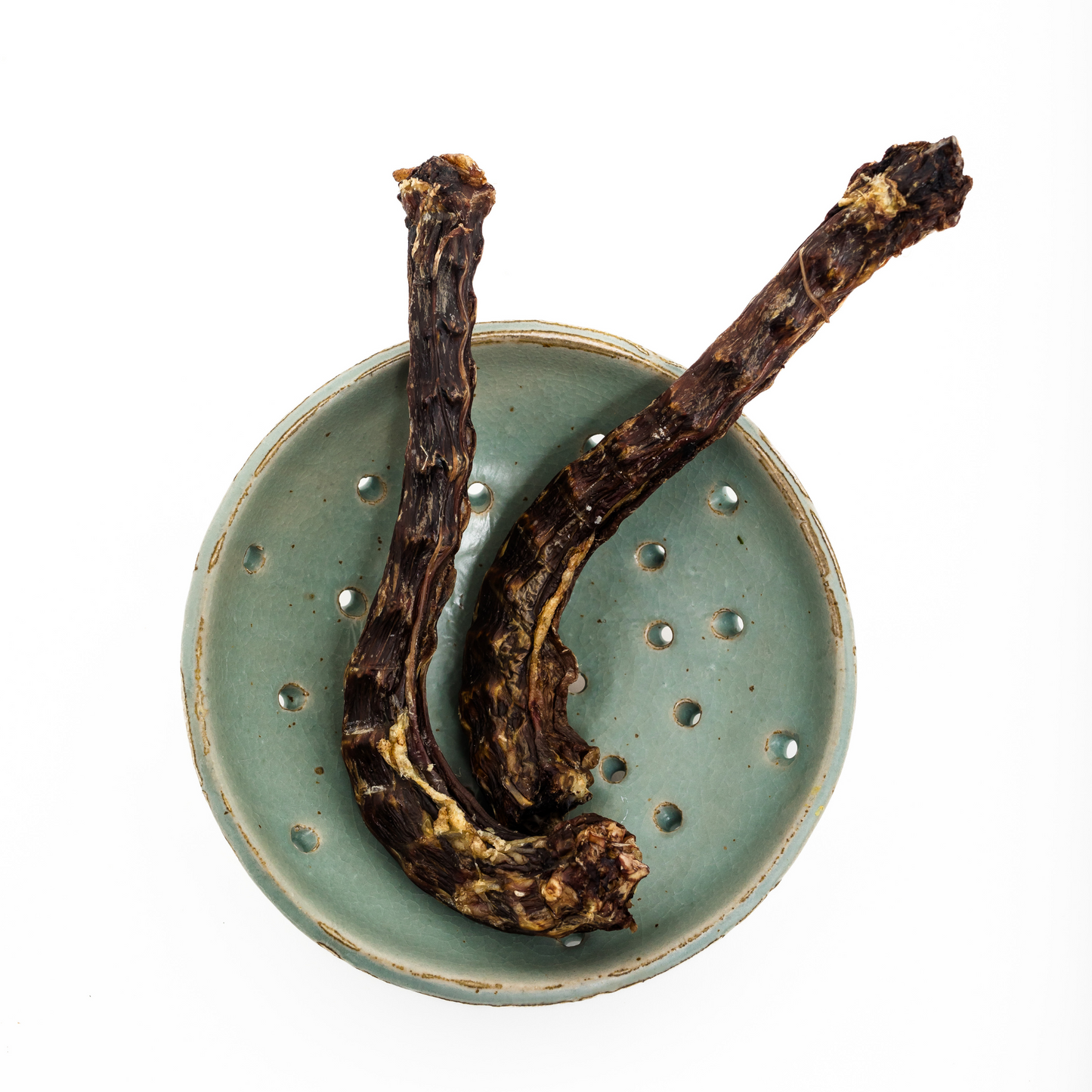 Two Dehydrated Goose Necks from Wild Nosh Pets, high in protein, are displayed on a green ceramic plate with holes against a white background.