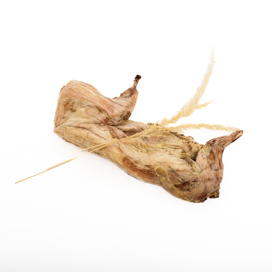 A Wild Nosh Pets Freeze-Dried Half Rabbit is displayed on a white surface with dried grass—a genuine treat sourced from our family farm.