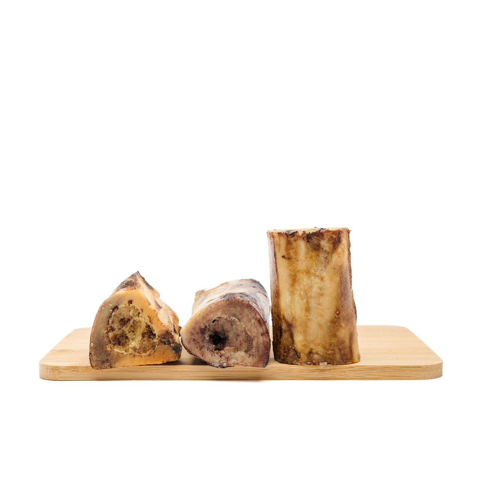 Three large Wild Nosh Pets Smoked Bison Marrow Bones, including two halved and one whole, presented on a wooden cutting board—ideal for cleaning teeth and gums.