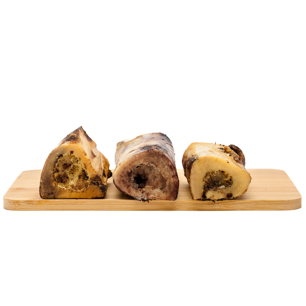 Three large Wild Nosh Pets Smoked Bison Marrow Bones with hollow centers are displayed on a wooden cutting board, showcasing a variety of textures and colors. Ideal for cleaning teeth and gums, these bones offer a long-lasting chew.