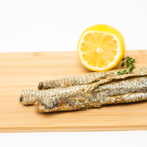 A few Wild Nosh Pets Carp Skin Rolls rich in omega fatty acids are placed on a wooden cutting board next to a partially sliced lemon.