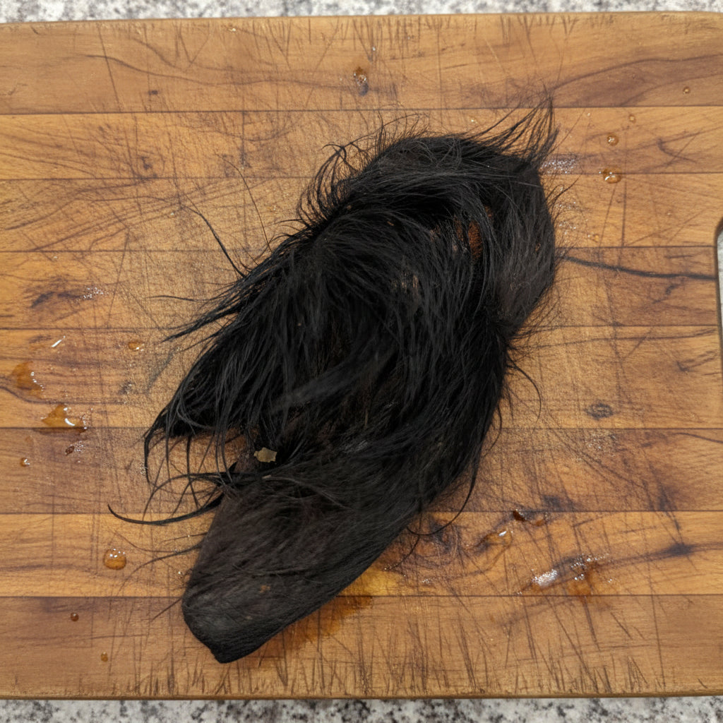 A dehydrated, hairy bison ear from Wild Nosh Pets on a wooden board with droplets—a natural dog chew crafted to support joint health.