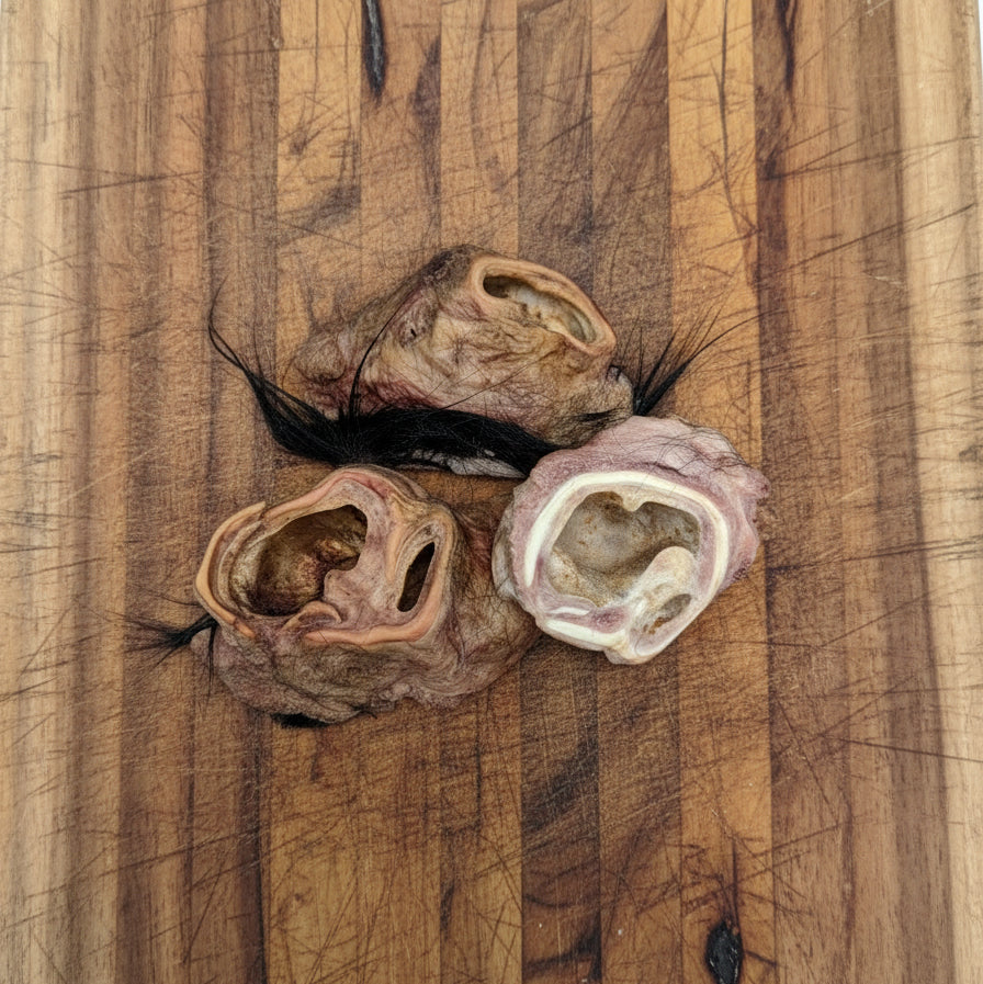 Three Wild Nosh Pets Hairy Bison Ear Buds with visible fur tufts are displayed on a scratched wooden cutting board, providing a natural protein source for pets.