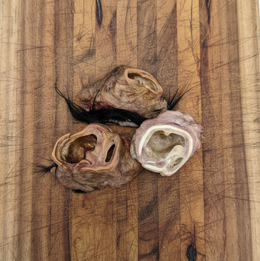 Three Wild Nosh Pets Hairy Bison Ear Buds with visible fur tufts are displayed on a scratched wooden cutting board, providing a natural protein source for pets.