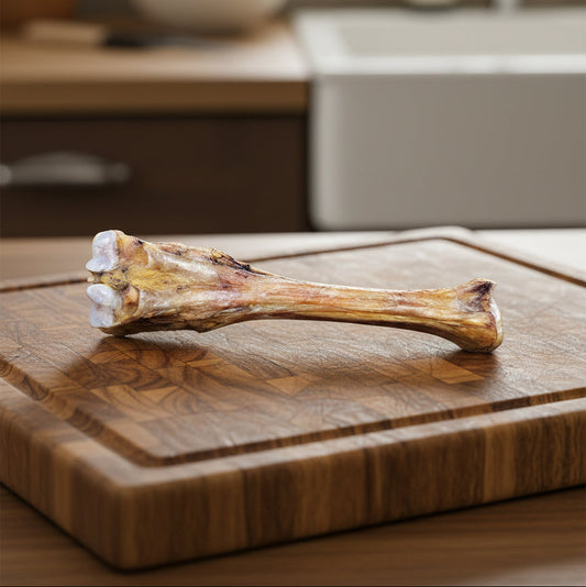 The Wild Nosh Pets Slow Roasted Bison Trotter Bone—Limited Edition, Field Harvested, and 100% Grass Finished—makes a natural dog chew treat, shown resting on a wooden cutting board in the kitchen.