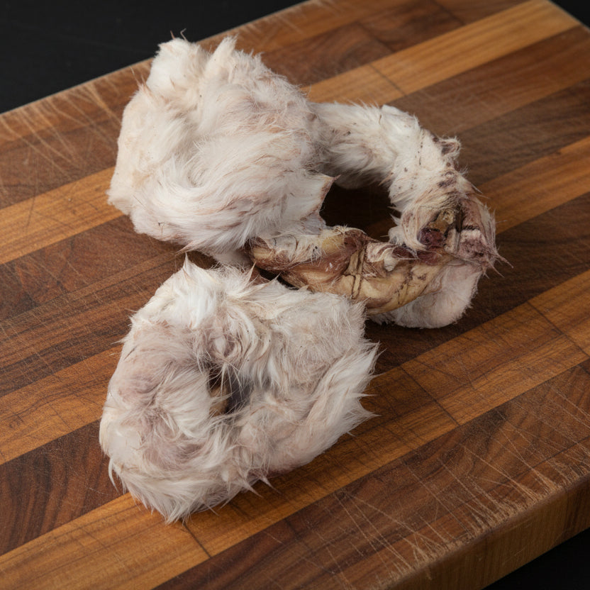 Three Rabbit Hide Donuts by Wild Nosh Pets, featuring fur and natural textures, are displayed on a scratched white surface.